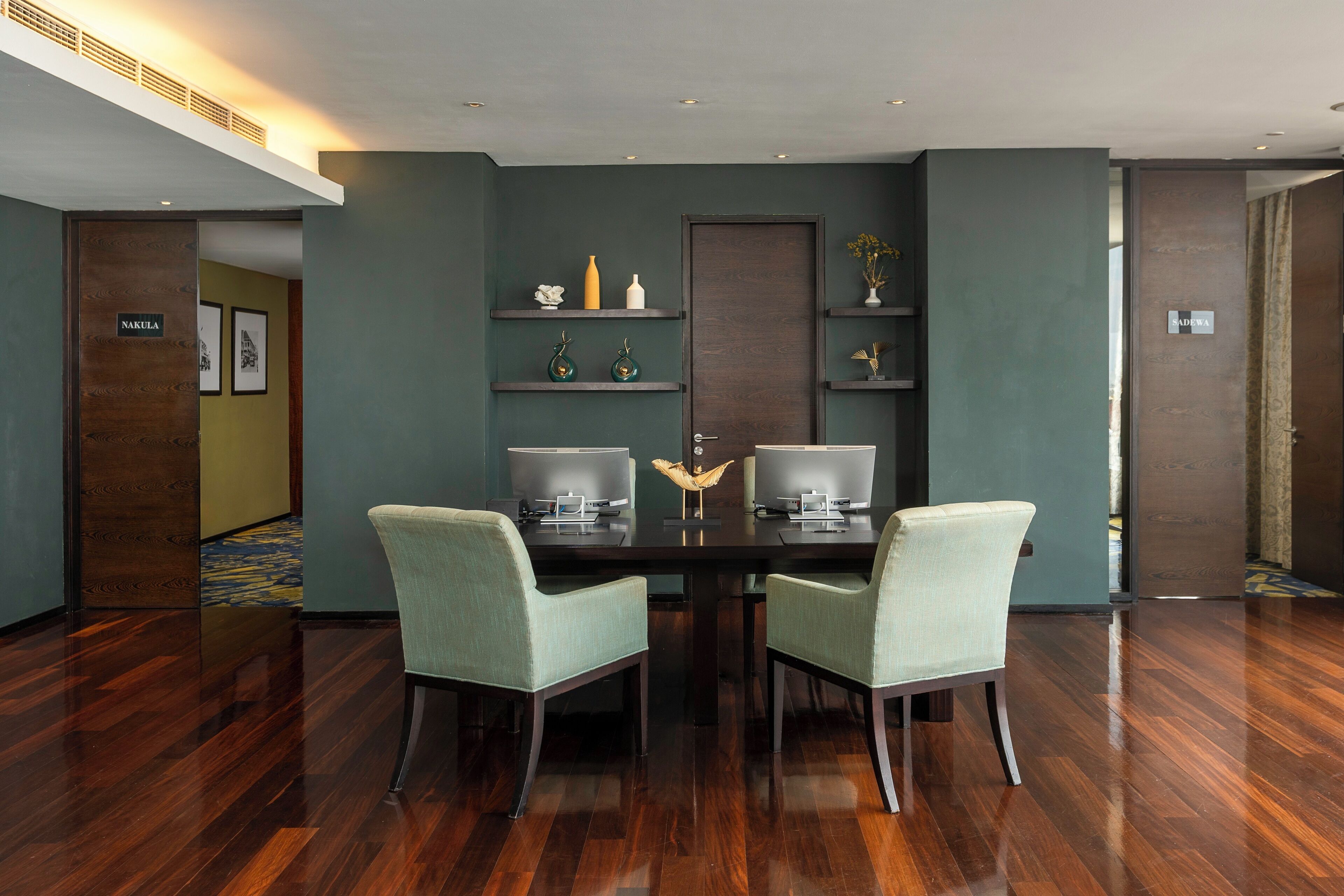 Un salón de conferencias con una mesa de madera oscura, dos sillas verde claro y una decoración moderna con estantes empotrados.