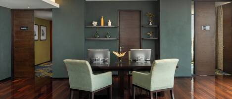Un salón de conferencias con una mesa de madera oscura, dos sillas verde claro y una decoración moderna con estantes empotrados.