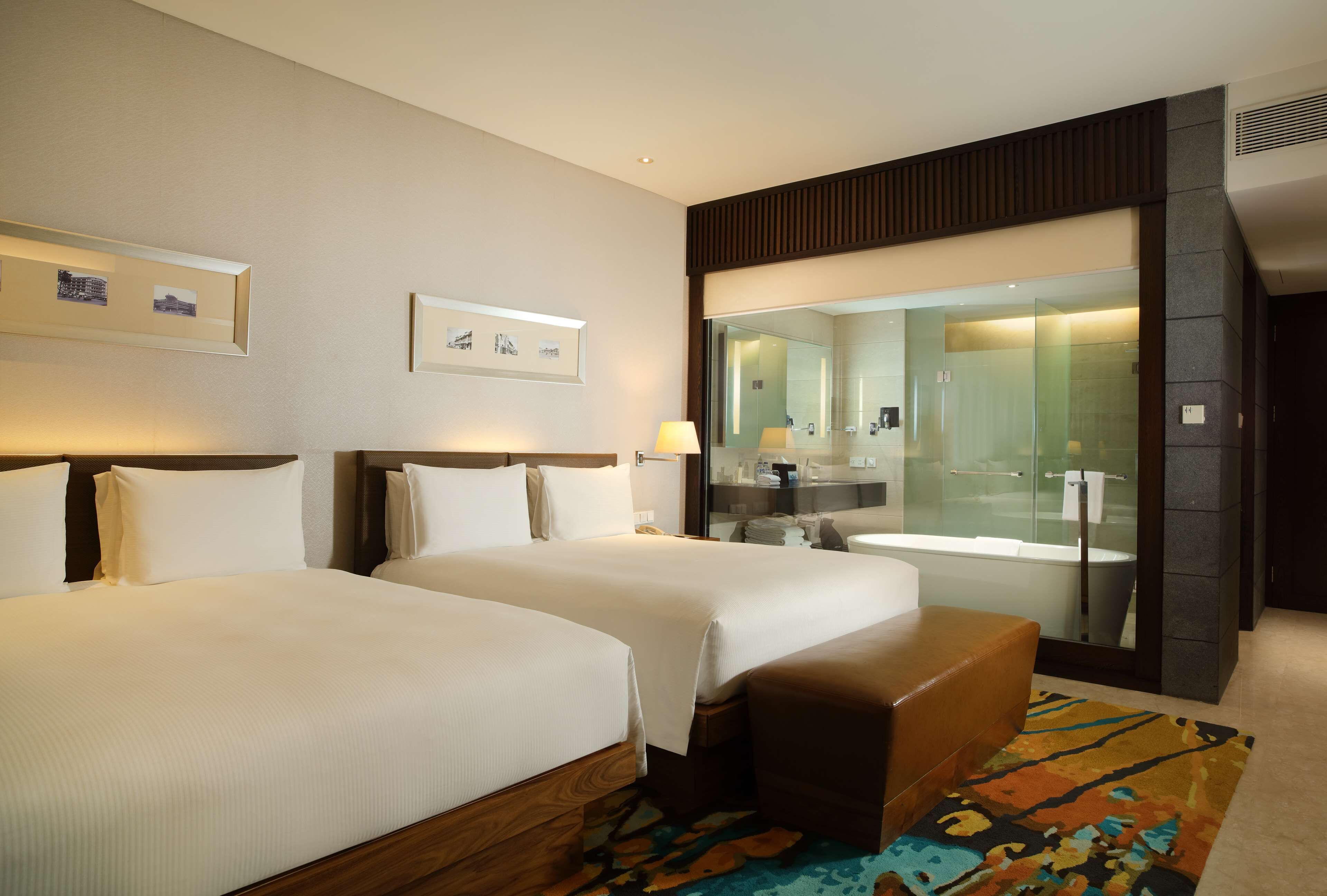 A hotel room with two beds, a bathroom with a glass shower, and a large mirror.