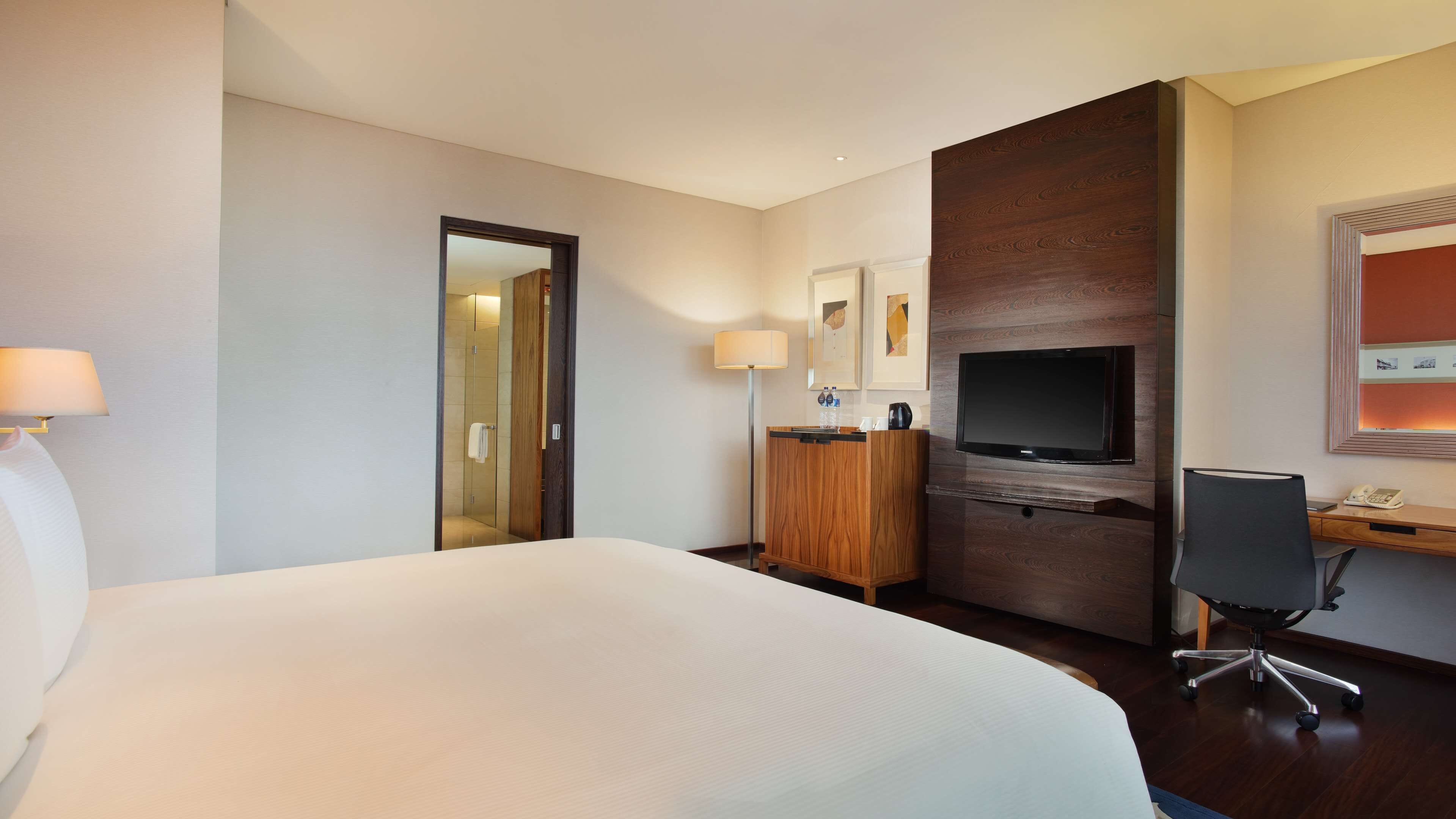 Habitación de hotel con una cama grande, un escritorio con silla, televisor, espejo y armario.