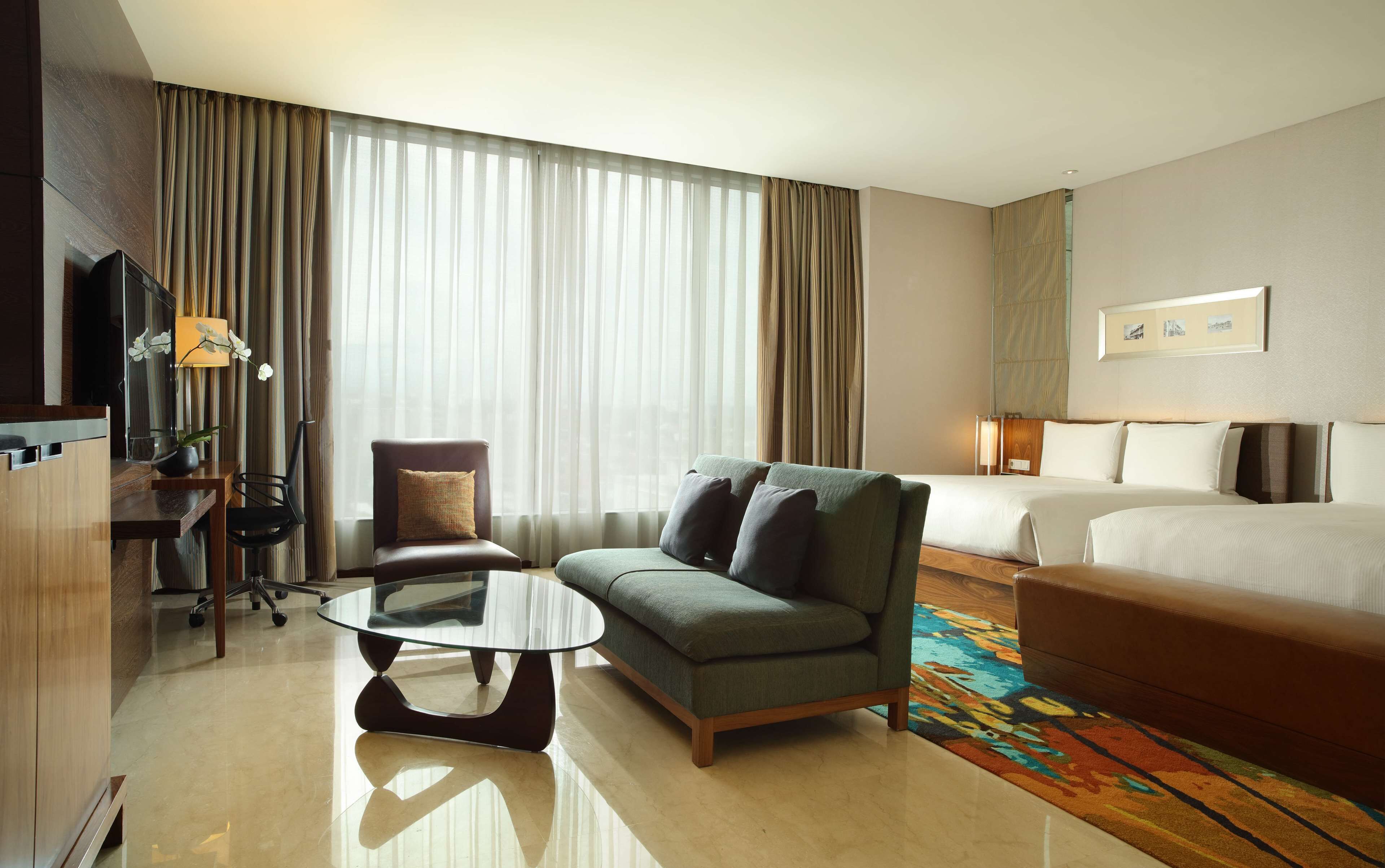 A hotel room with a bed, a sofa, a chair, a small table, and a TV.
