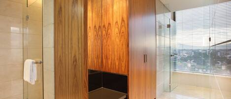 A modern bathroom with a glass shower enclosure, wooden cabinetry, and a view of the city through large windows.