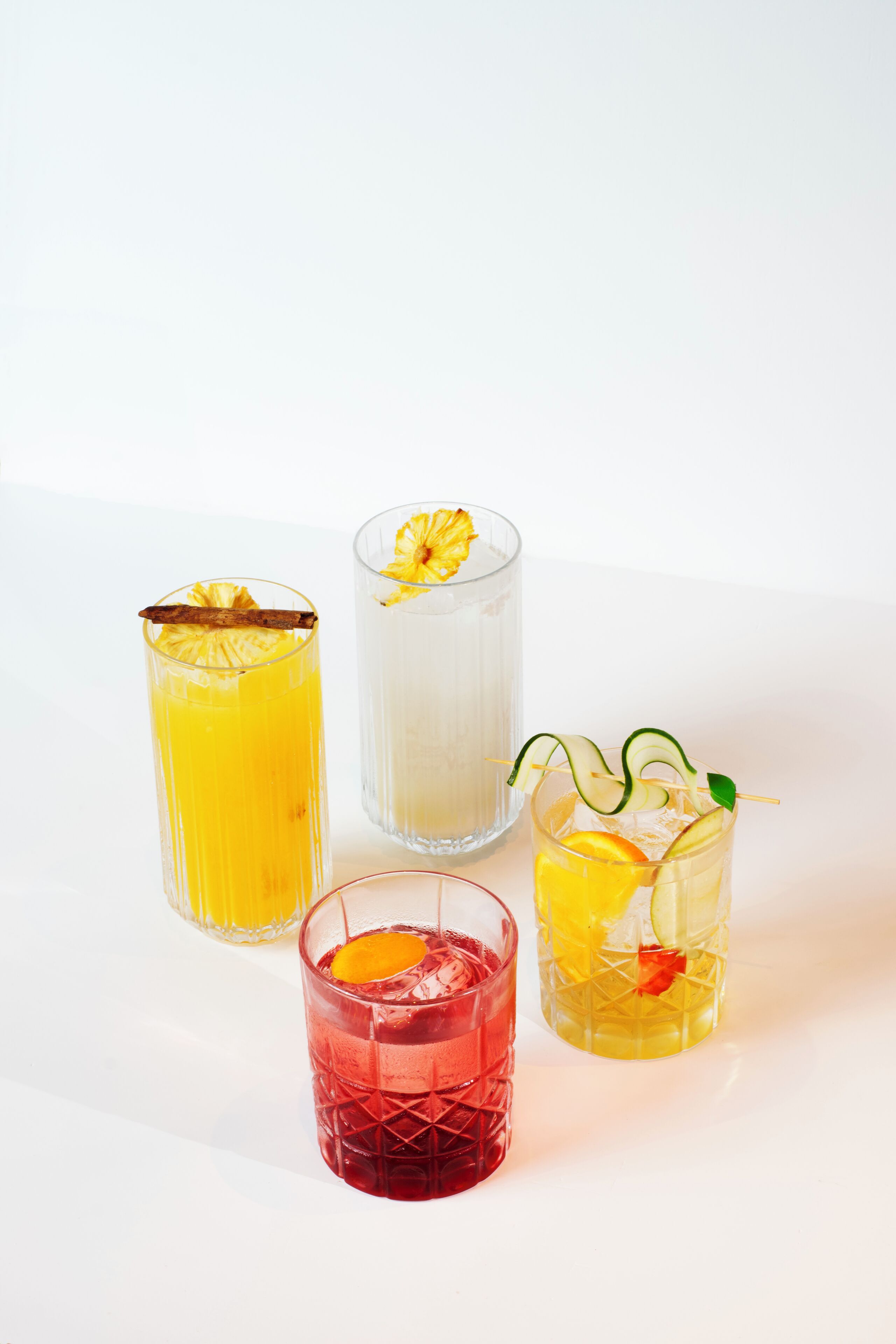Four glasses of different beverages with garnishes.