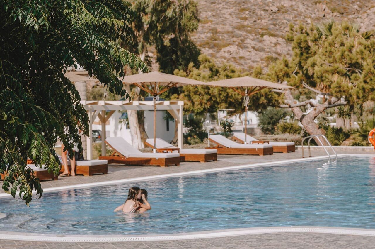 A swimming pool with lounge chairs and umbrellas, surrounded by trees and a mountainous backdrop.