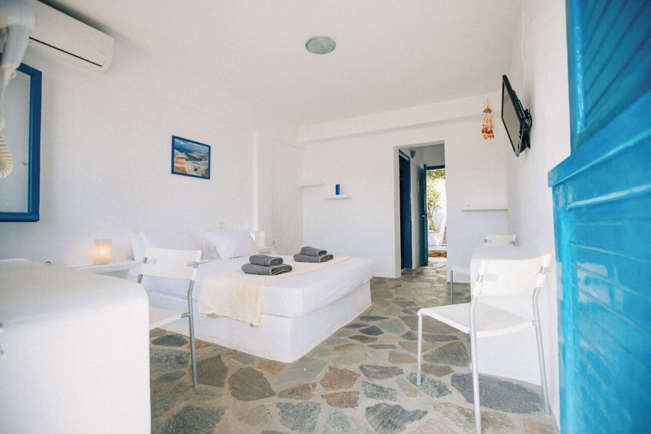 Una habitación con una cama, una silla y una pequeña mesa. Hay un cuadro en la pared y una ventana.