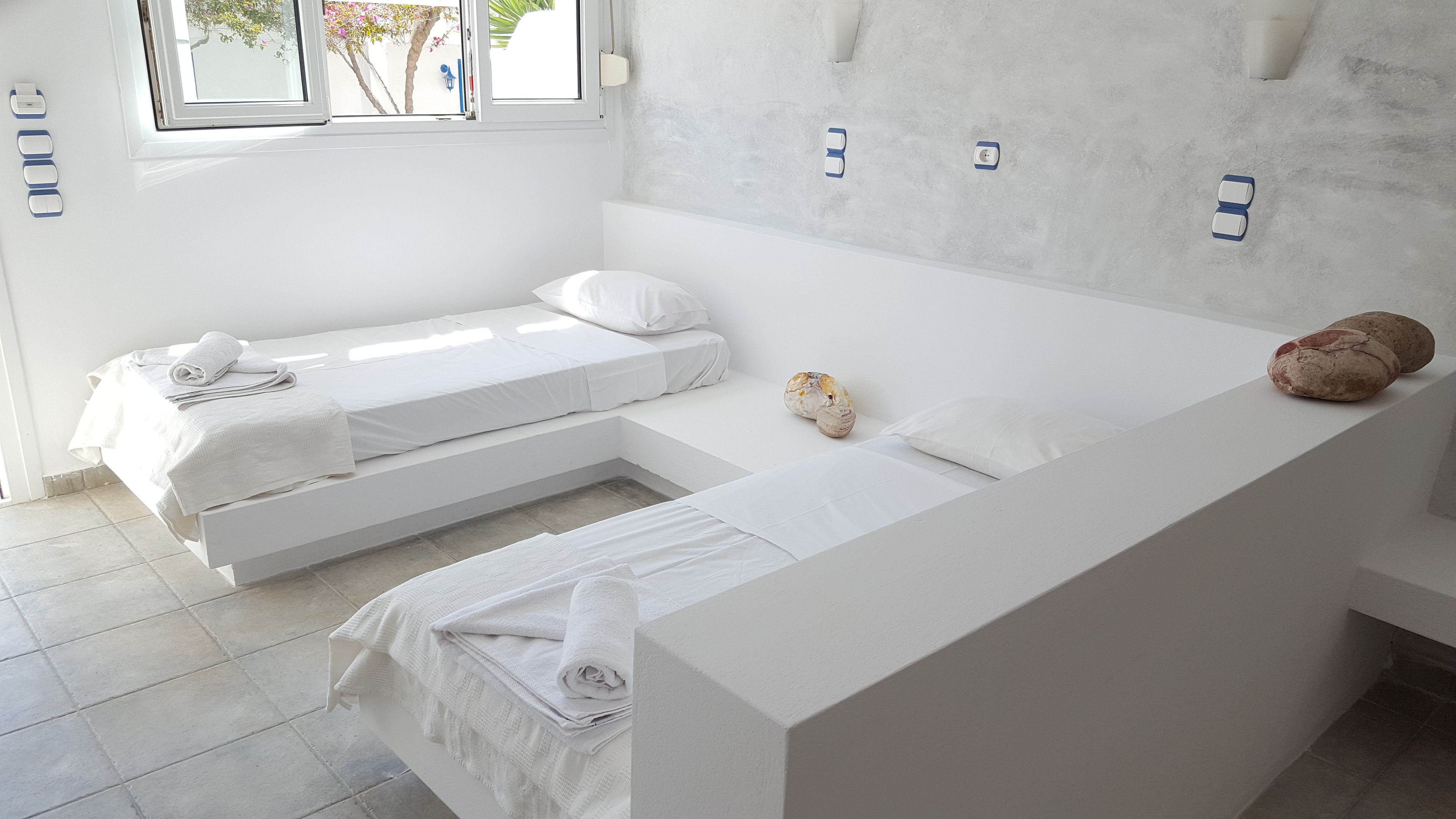 A modern, minimalist bedroom with two single beds, a large window, and a bathroom with a bathtub.