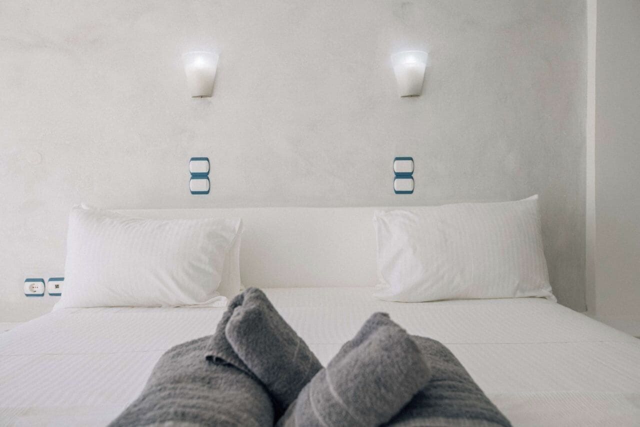 Una cama con ropa de cama blanca y dos lámparas de pared.