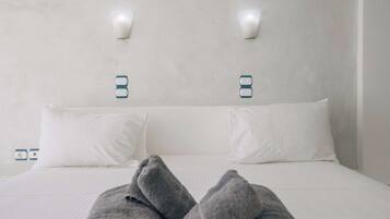 Una cama con ropa de cama blanca y dos lámparas de pared.