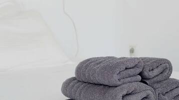 En pænt redt seng med foldede håndklæder og en stikkontakt på væggen.