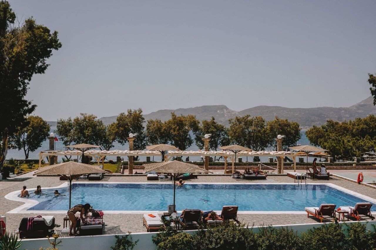 A pool area with lounge chairs and umbrellas, surrounded by trees and a view of mountains.