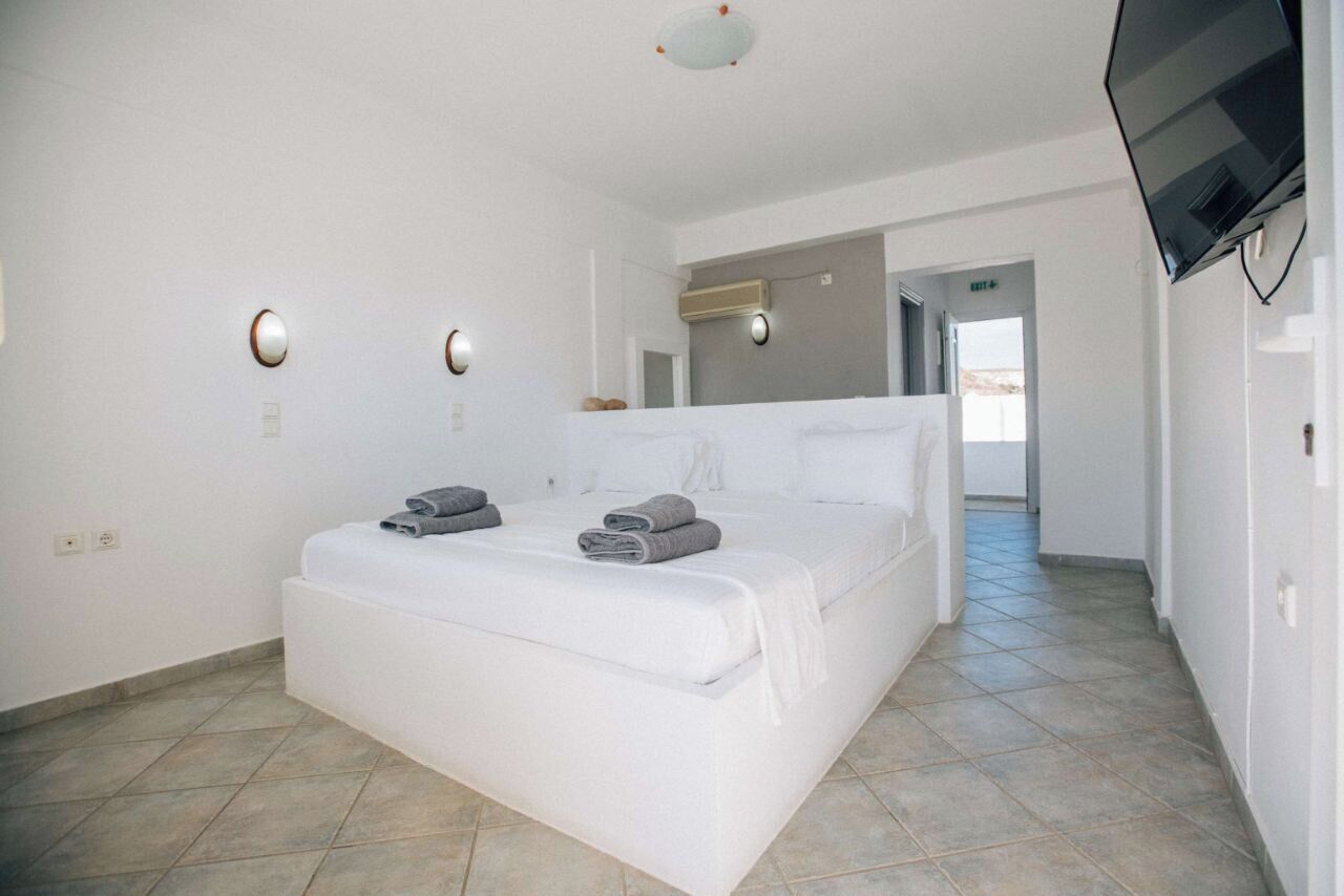 A hotel room with a large bed, a flat-screen TV mounted on the wall, and a hallway leading to another room.