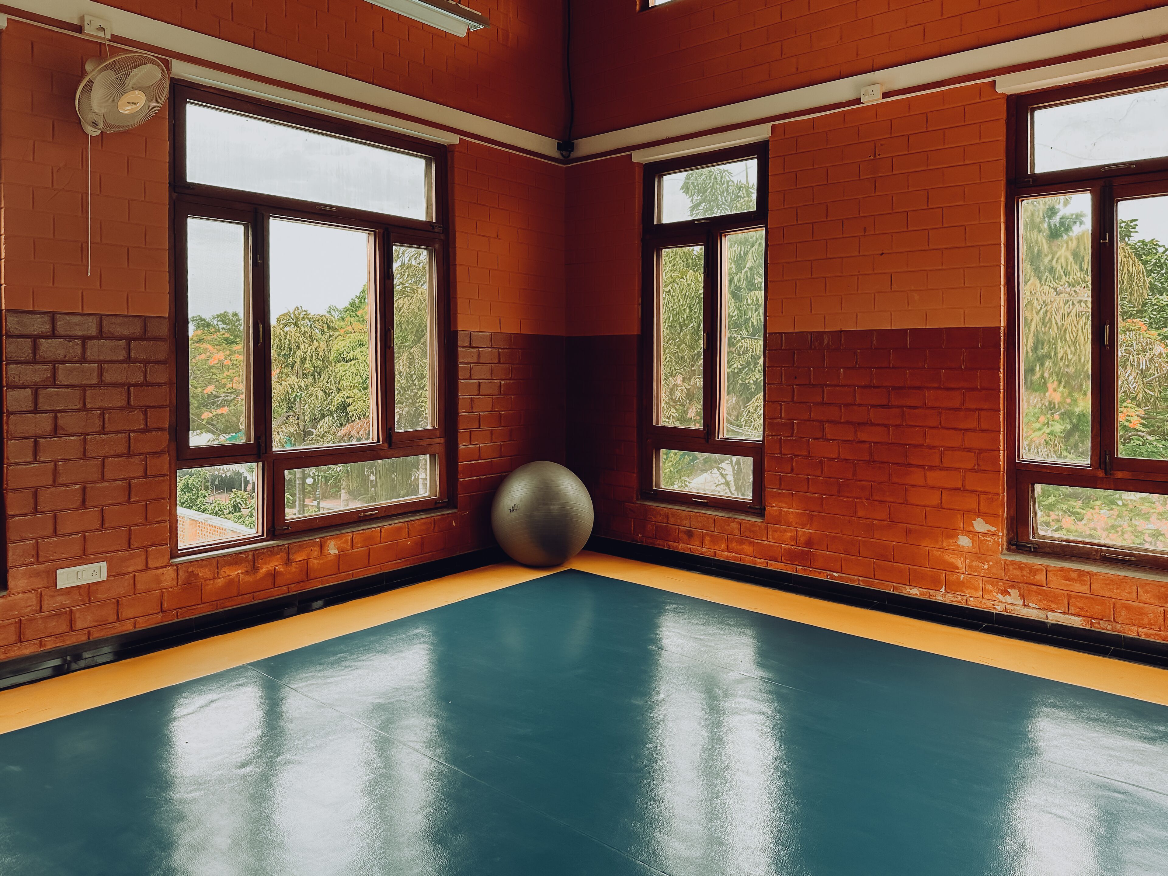 A gym with brick walls, large windows, and a blue floor.
