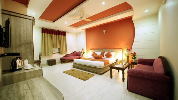 A modern hotel room with a large bed, a seating area with a sofa and armchairs, a coffee table, and a television. - Hotel Blue Bell (New Delhi)