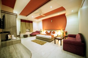 A modern hotel room with a large bed, a seating area with a sofa and armchairs, a coffee table, and a television. - Hotel Blue Bell (New Delhi)
