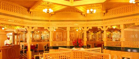 A restaurant with a high ceiling, ornate ceiling design, chandeliers, and red tablecloths.