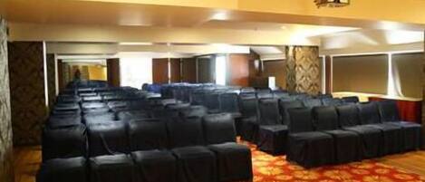 Un salón de conferencias con filas de sillas negras, una alfombra estampada y una araña de cristal.