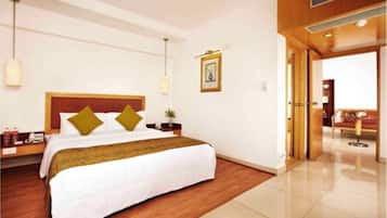 Habitación de hotel con una cama grande, suelo de madera, una mesita de noche, una lámpara y un cuadro en la pared.