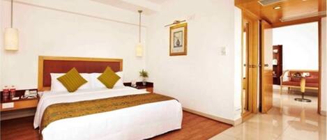 A hotel room with a large bed, wooden floor, a nightstand, a lamp, and a framed picture on the wall.