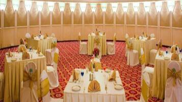 Une salle de banquet avec des tables rondes, chacune recouverte d’une nappe blanche et ornée d’un ruban doré, disposées en cercle.
