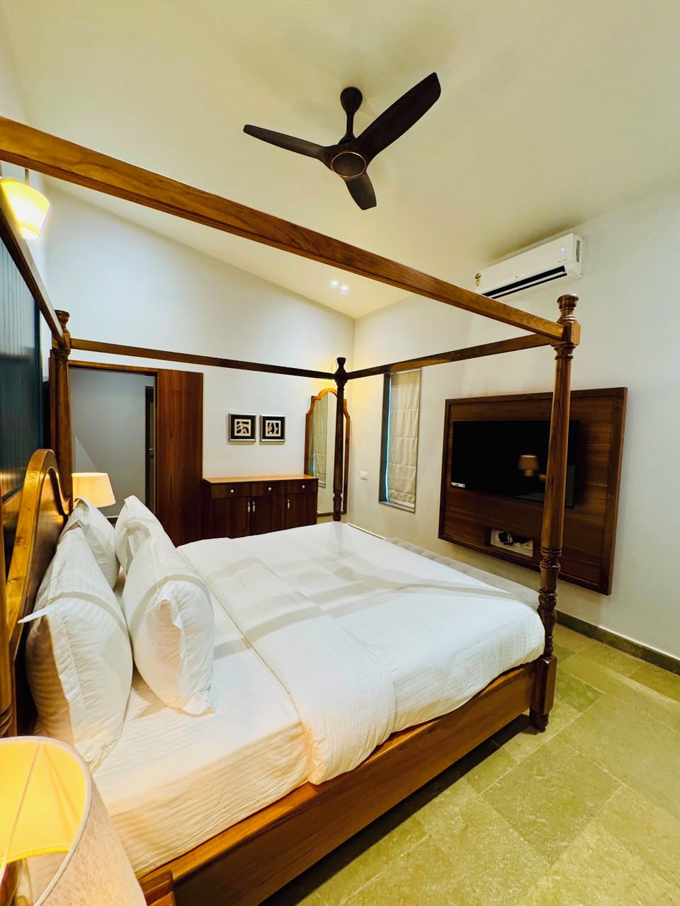 A four-poster bed with a ceiling fan, a flat-screen TV, and a wooden cabinet.