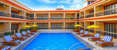 A multi-level hotel with a central swimming pool, sun loungers, and yellow umbrellas.