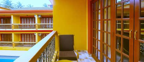 Un balcón con una mesa y una silla amarillas, una piscina y un edificio con múltiples ventanas y balcones.