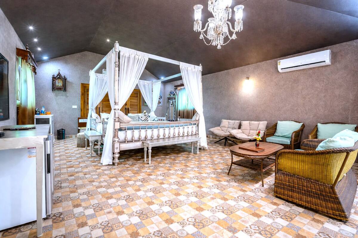 Quarto com cama de dossel, lustre, mobiliário de vime e piso estampado.