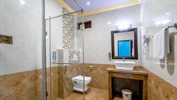 Une salle de bain moderne avec une douche à parois de verre, des toilettes blanches, un lavabo doté d’un plan de travail en marbre et un miroir avec un verre teinté en bleu.