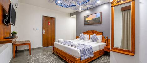 A hotel room with a bed, a desk, a chair, a mirror, and a ceiling light fixture.