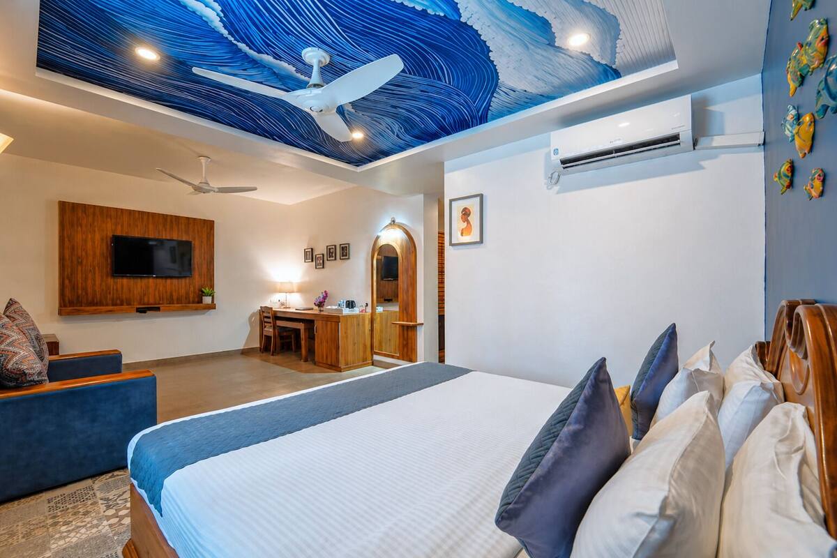 Quarto de hotel moderno com uma cama grande, uma mesa de escritório, uma TV e um mural no teto.