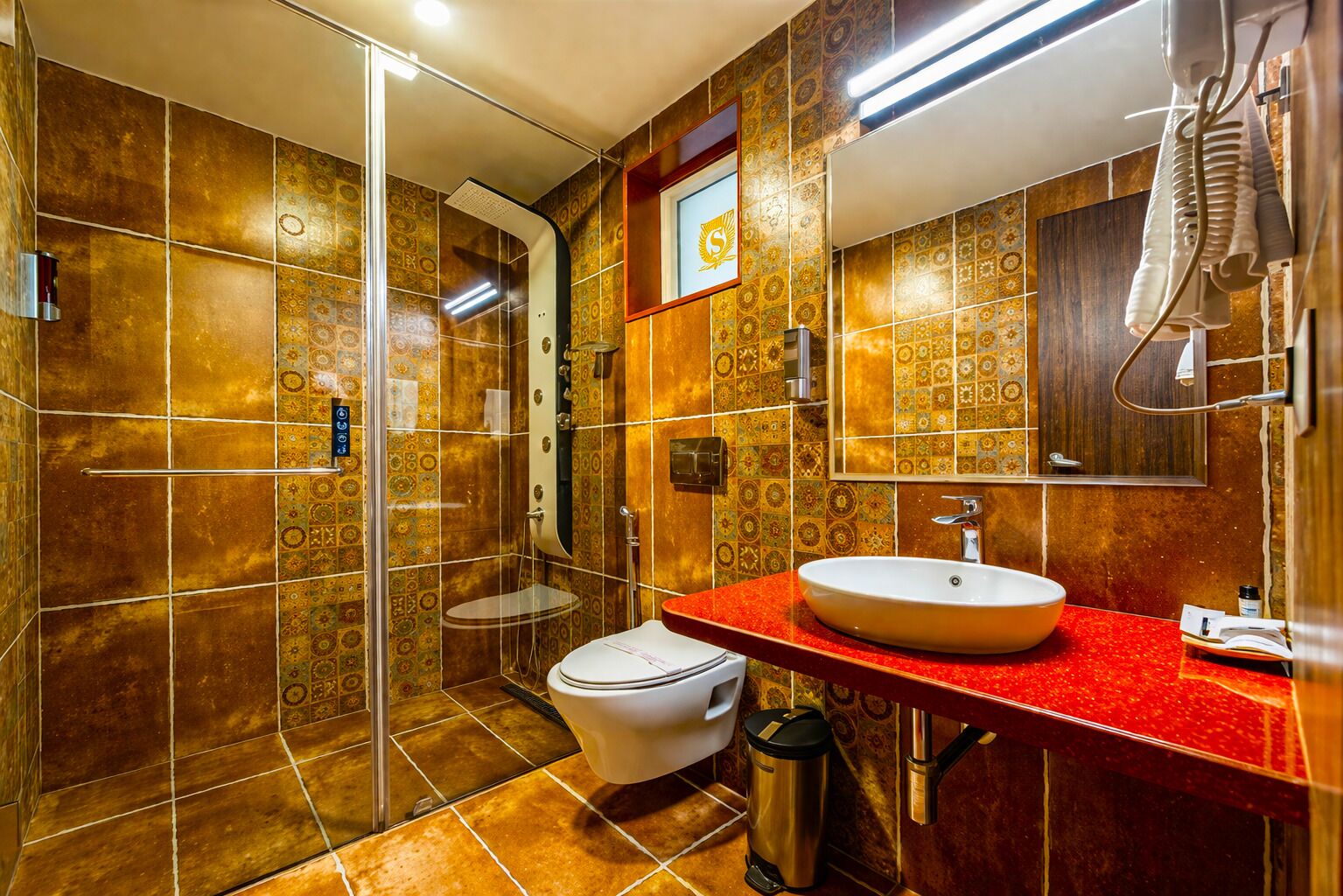 A bathroom with a shower, toilet, and sink, featuring patterned tiles and a red countertop.