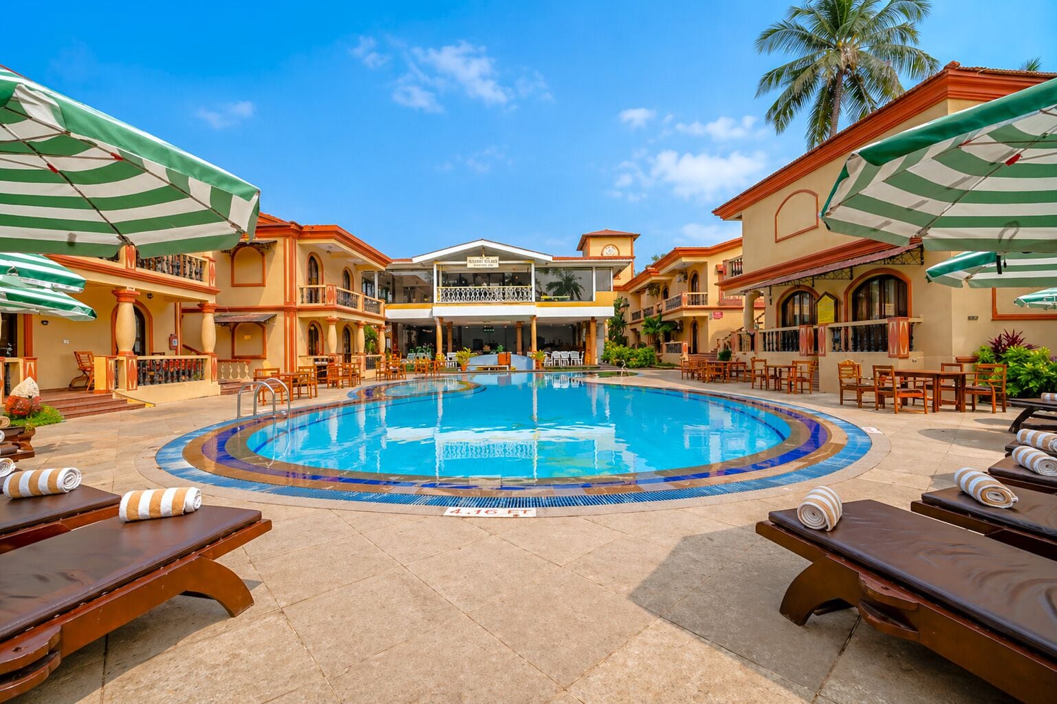 A swimming pool with lounge chairs and umbrellas, surrounded by buildings with balconies and outdoor seating.