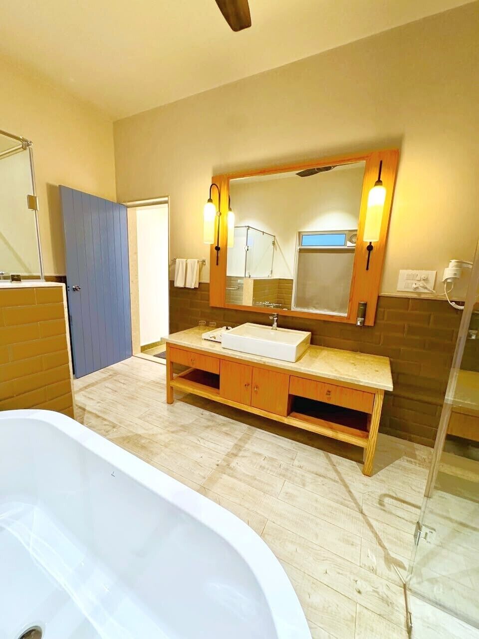 A bathroom with a bathtub, a wooden vanity with a sink, a large mirror with wall sconces, and a shower area.