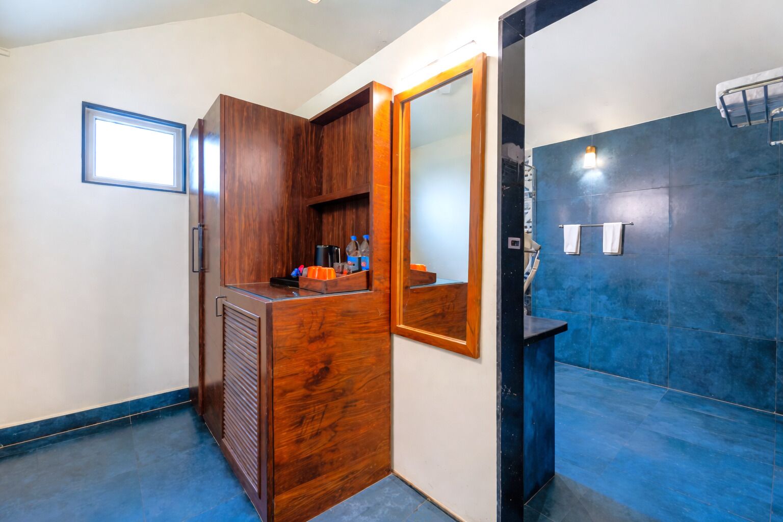 A bathroom with a wooden vanity, a mirror, a towel rack, and blue-tiled walls.