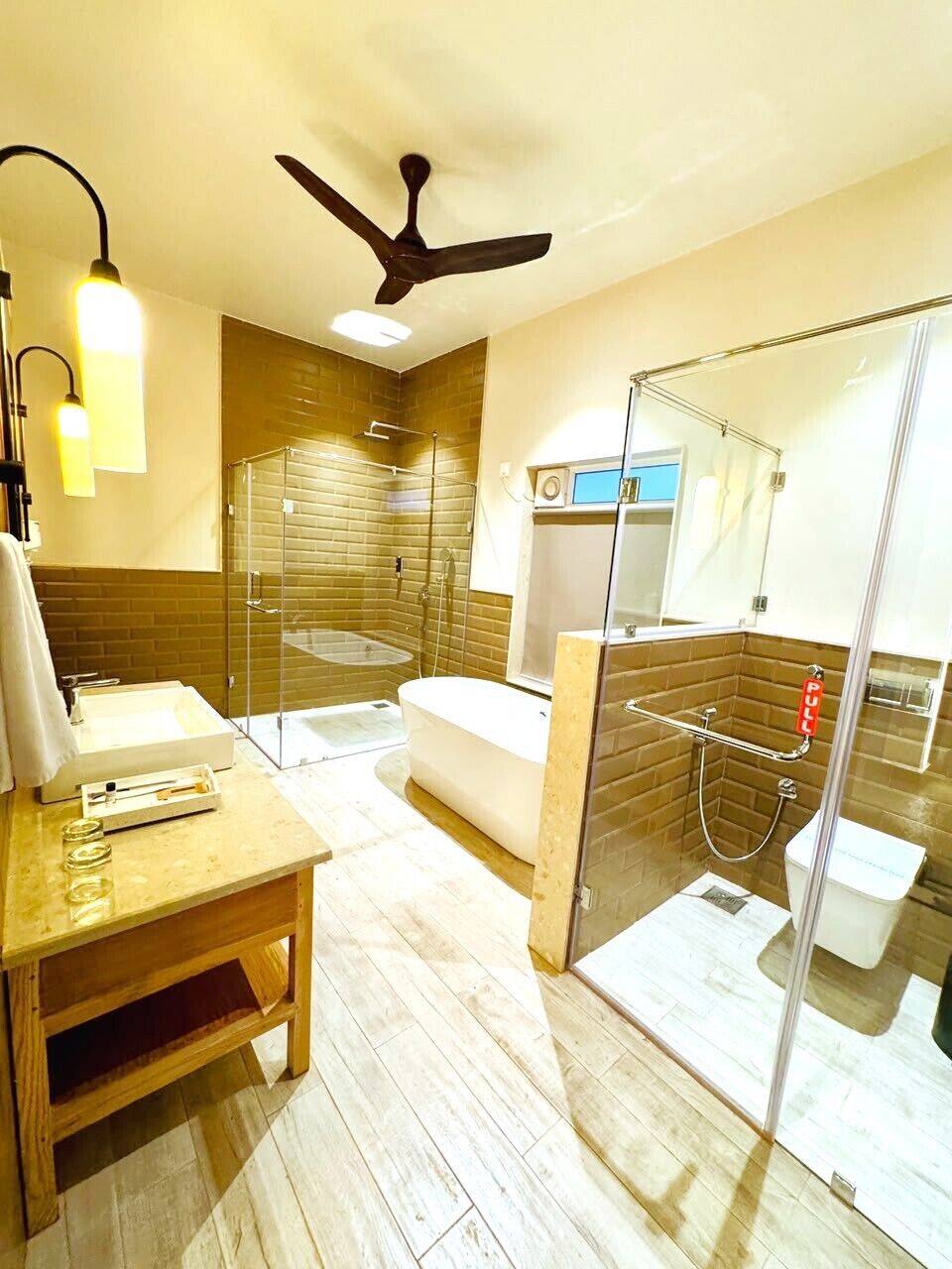 Un baño moderno con ducha de vidrio, tocador de madera y ventilador de techo.