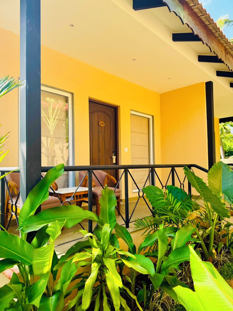 A yellow building with a covered porch, a door, and a railing.