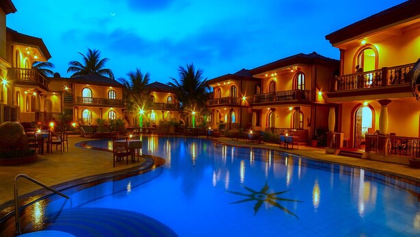 A hotel with a swimming pool, multiple balconies, and outdoor seating areas. - Resort Terra Paraiso (Calangute)
