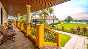 A covered outdoor seating area with chairs, a pool, and a view of a building and greenery. - Resort Terra Paraiso (Calangute)