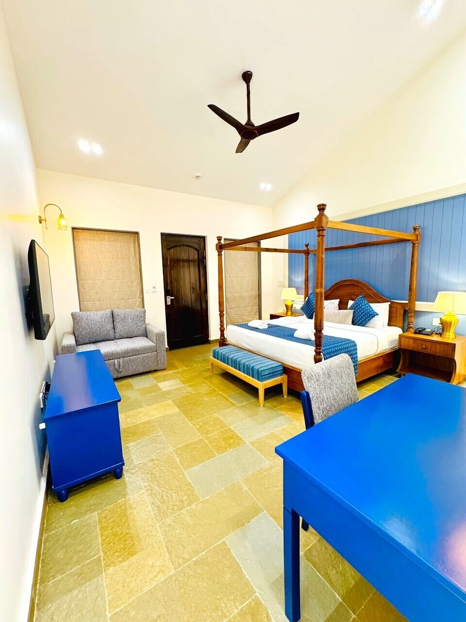 A hotel room with a four-poster bed, a sofa, a desk, and a ceiling fan.
