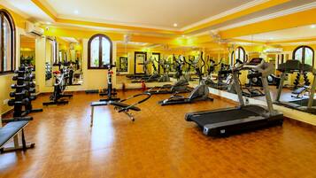 A gym with various exercise equipment, including treadmills and weight machines, and large mirrors on the walls.