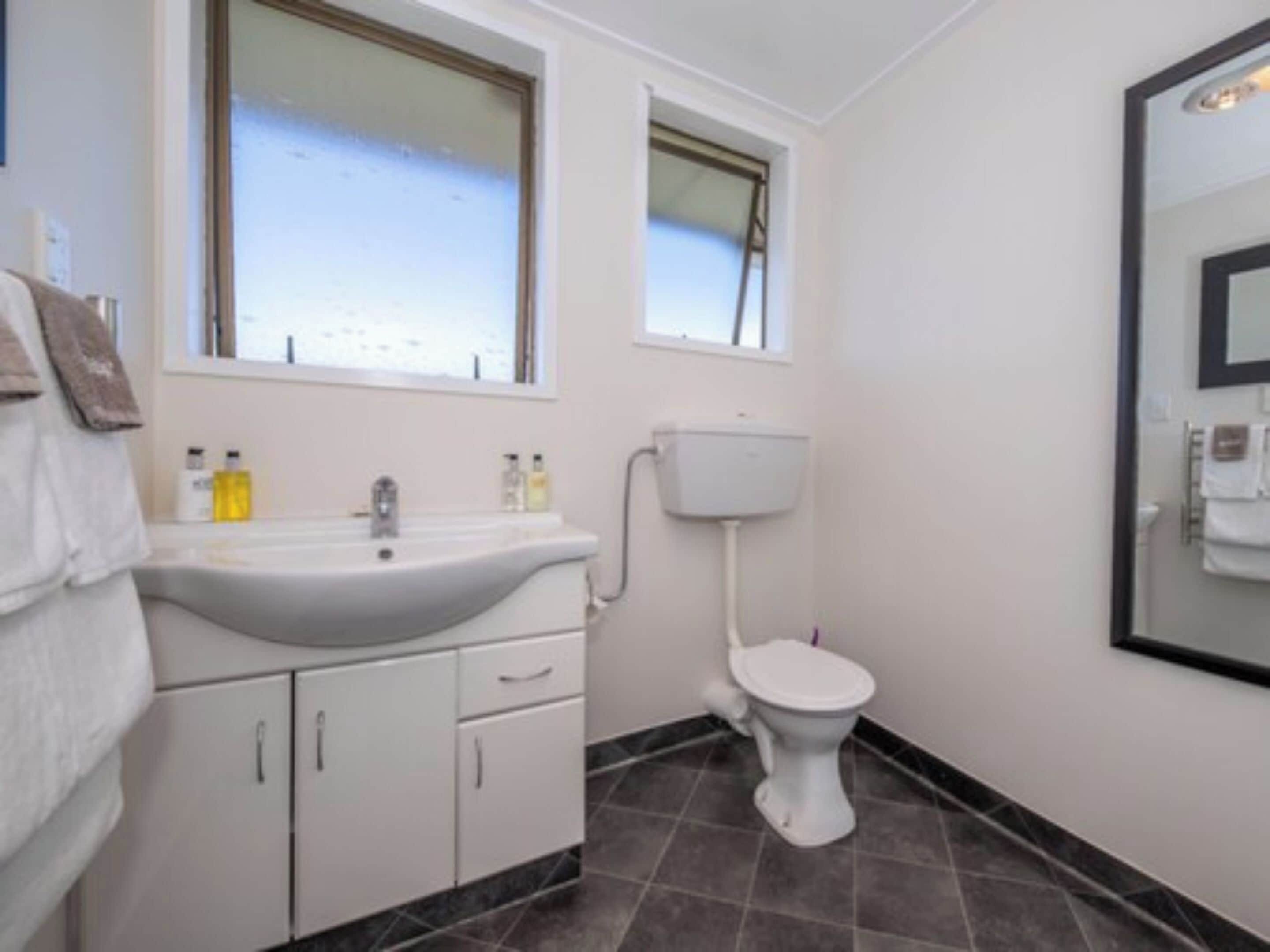 Un baño con lavamanos blanco, inodoro y ventana sobre el lavamanos.