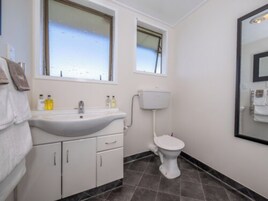 Un baño con lavamanos blanco, inodoro y ventana sobre el lavamanos.