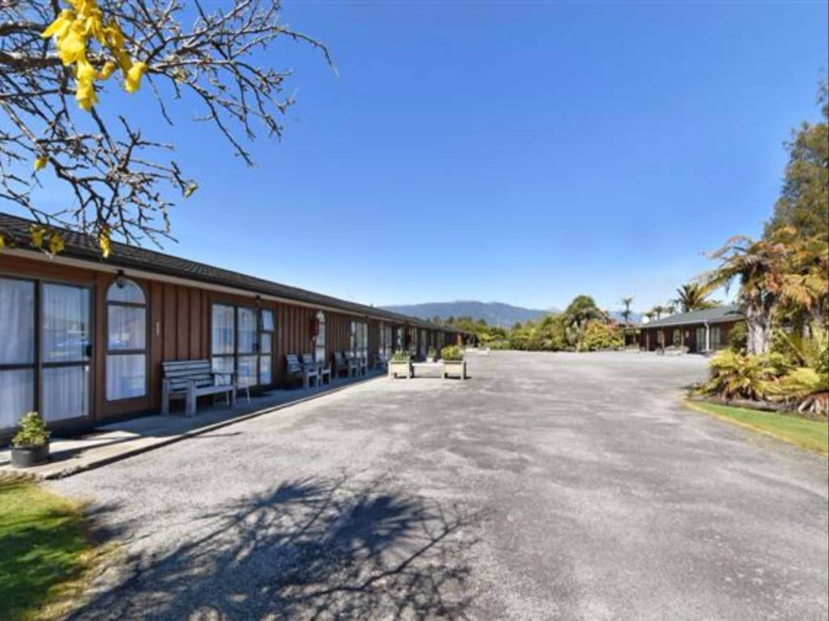 A motel with a long driveway, outdoor seating, and a mountain backdrop.