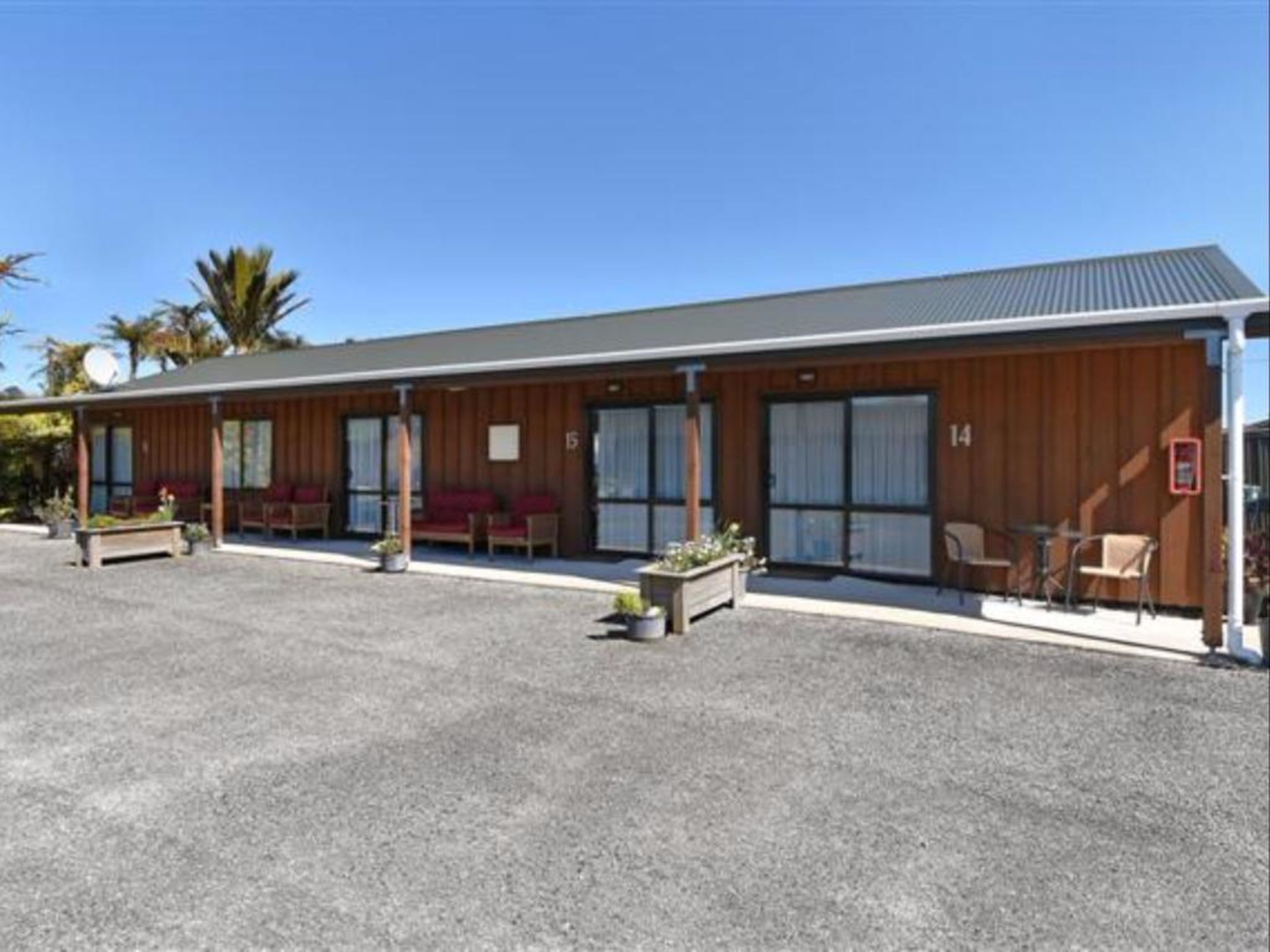 A motel with a covered outdoor seating area, a gravel driveway, and a wooden facade.