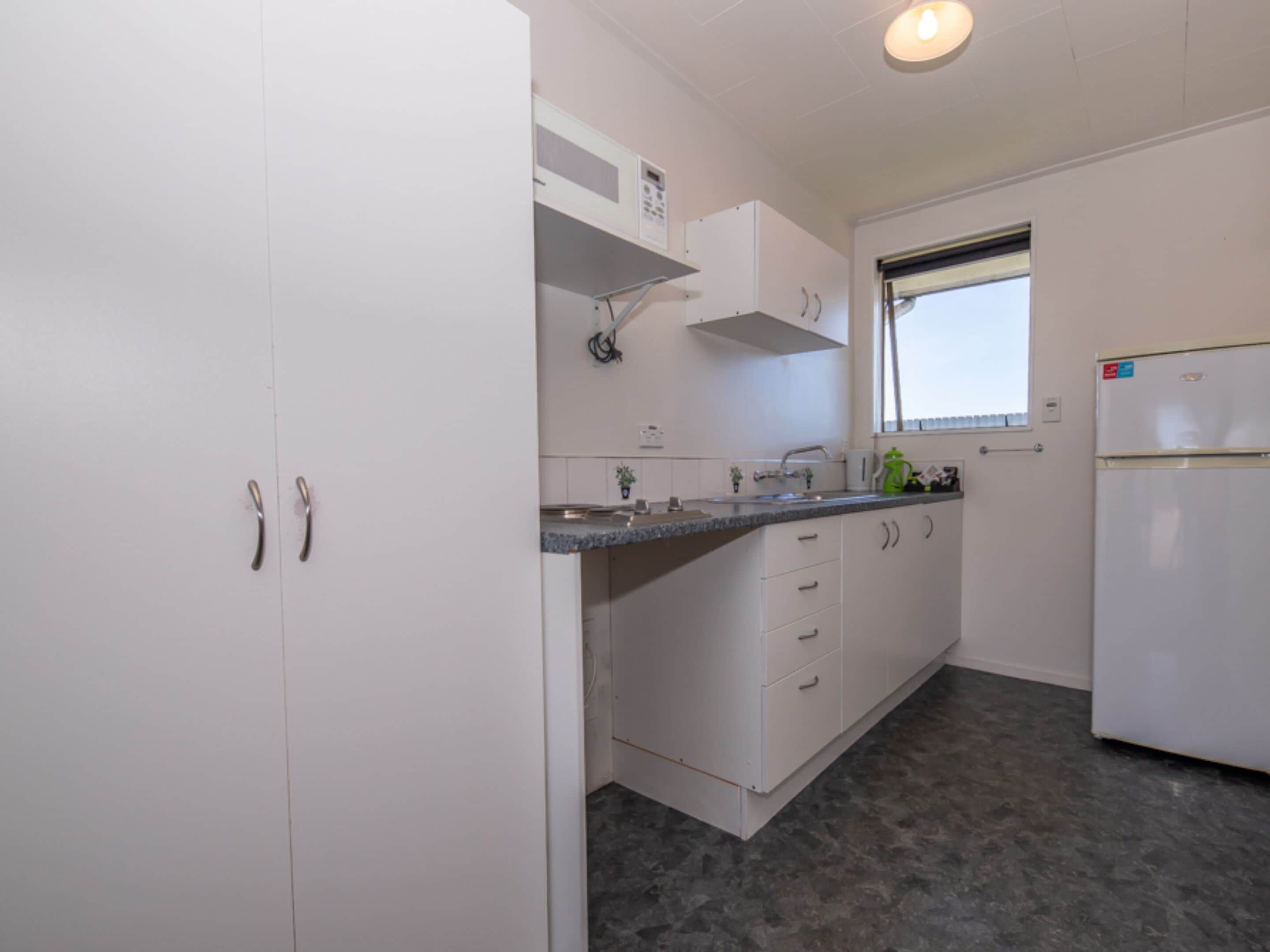 A compact kitchen with white cabinets, a granite countertop, a built-in oven, and a window with blinds.
