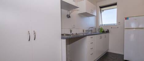 A compact kitchen with white cabinets, a granite countertop, a built-in oven, and a window with blinds.