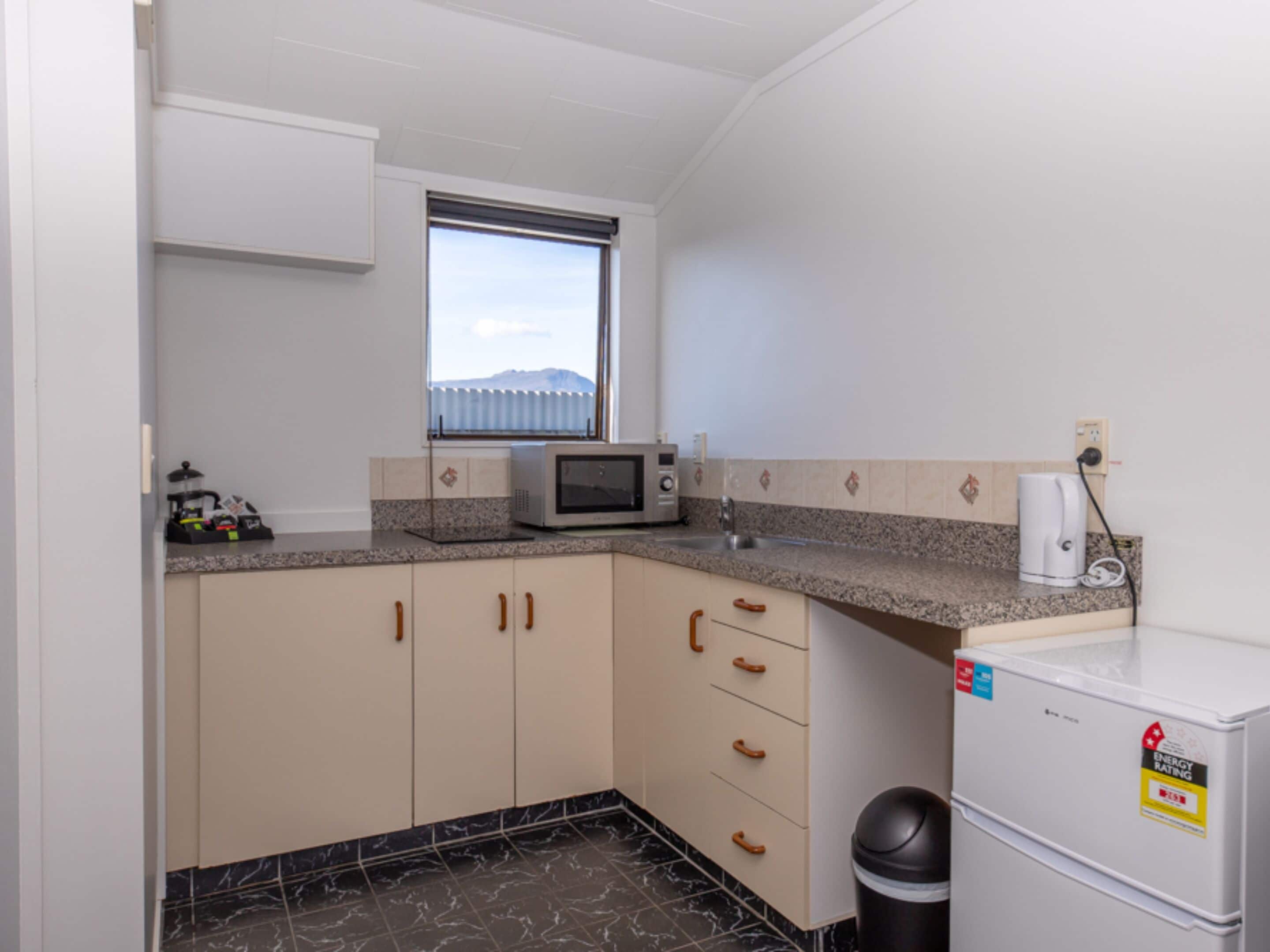 Uma cozinha compacta com micro-ondas, um frigorífico pequeno e uma janela com vista para uma montanha.