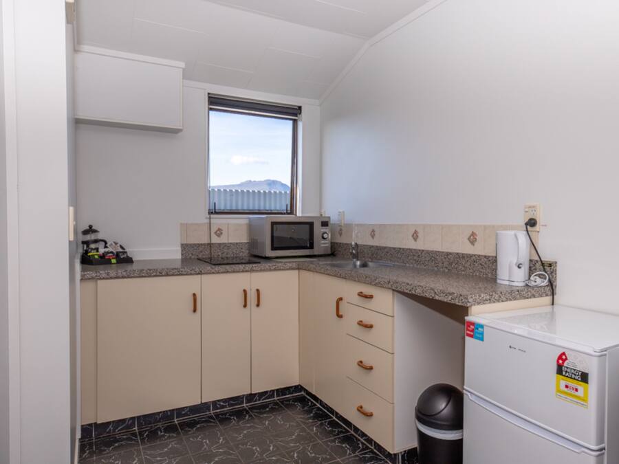 Uma cozinha compacta com micro-ondas, um frigorífico pequeno e uma janela com vista para uma montanha.
