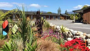 A hotel with a parking lot, outdoor seating area, and a garden with various plants and flowers. - Buller Bridge Motel (Westport)