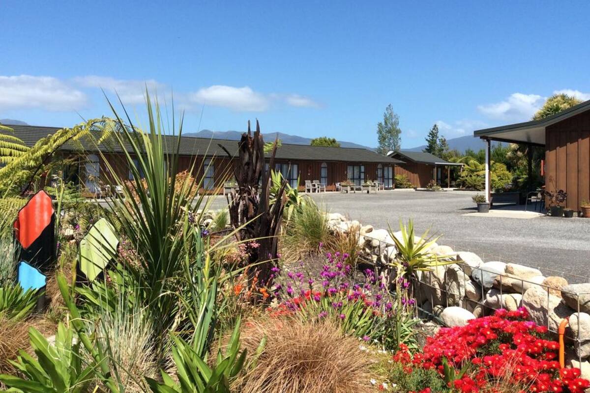 A hotel with a parking lot, outdoor seating area, and a garden with various plants and flowers.